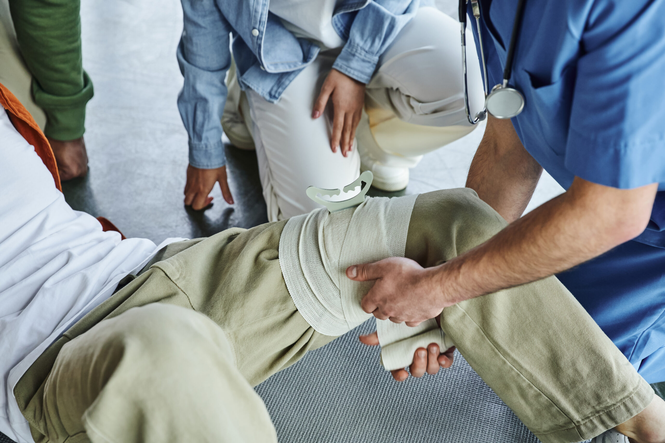 partial view of professional paramedic applying compressive bandage on leg of man near multiethnic group during first aid training seminar bleeding prevention techniques concept - Discover Tulsa Car Accident Injury Chiropractor