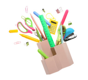 Flying holder with different stationery isolated on white background - Discover Tulsa Colorful office supplies including scissors, rulers, pencils, markers, paper clips, a stapler, and a calculator spilling out of a desk organizer on a white background.